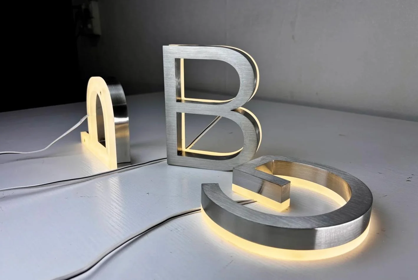 Brushed metal letters with illuminated acrylic backing on a work surface